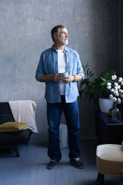 Yakışıklı son sınıf öğrencisi elinde bir kupa tutuyor, başka tarafa bakıyor ve dairede dururken gülümsüyor..