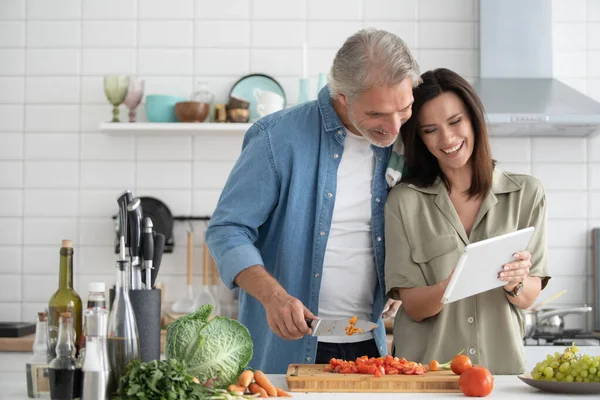 Beautiful couple using a digital tablet and smiling while cooking in kitchen at home.