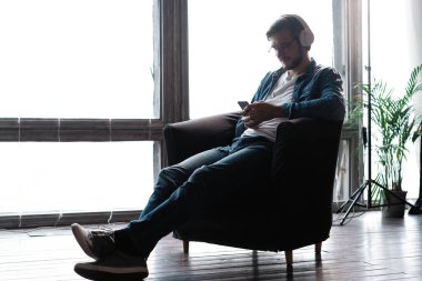 Kablosuz kulaklık takan gülümseyen genç bir adam akıllı telefondan cep telefonu müziği dinliyor.