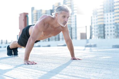 Orta yaşlı atletik bir adam dışarıda şınav çekiyor. Fitness ve açık hava kentsel ortamı.