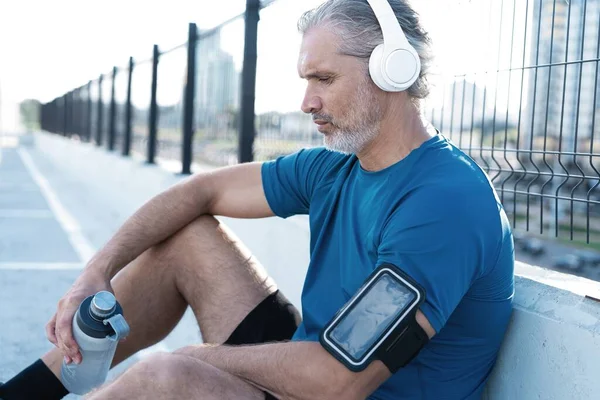 Cansado hombre de mediana edad agotado Descansando después de correr al aire libre. Guapo corredor tomando descanso después de entrenamiento de fitness — Foto de Stock