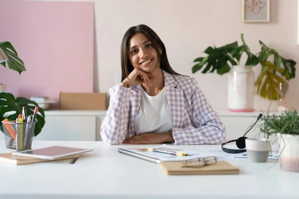 Retrato de una alegre mujer de negocios india de raza mixta sentada en la mesa de la oficina y mirando a la cámara. — Foto de Stock