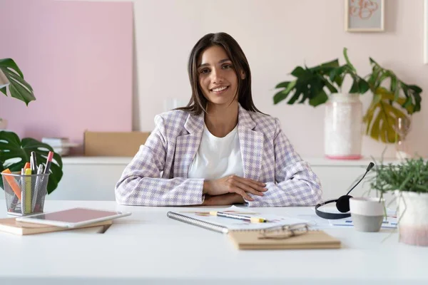 Retrato de una alegre mujer de negocios india de raza mixta sentada en la mesa de la oficina y mirando a la cámara. — Foto de Stock