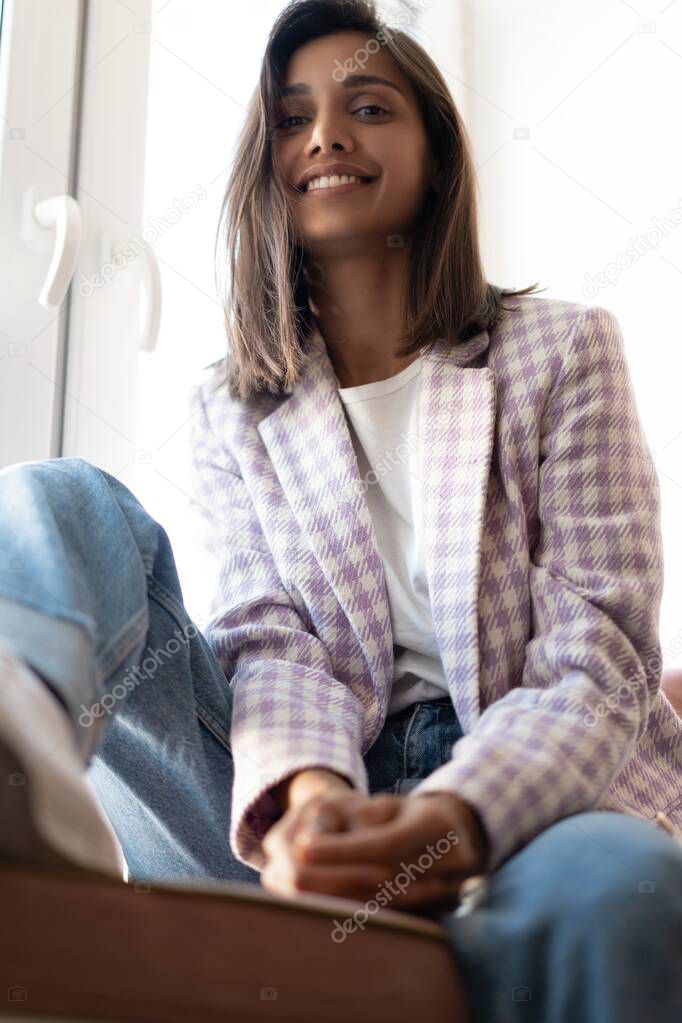 Young Indian mixed-race woman dressed casually sitting on the window sill at home office