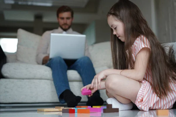 Freelance and fatherhood concept - father working on laptop while daughter playing on the floor at home — Stock Photo, Image