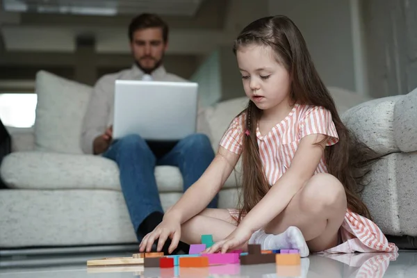 Concepto freelance y paternidad - padre que trabaja en el ordenador portátil mientras su hija juega en el suelo en casa —  Fotos de Stock