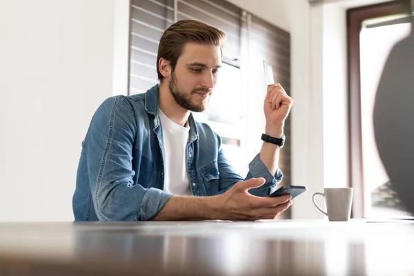 Homme confiant tenant un smartphone, assis dans la cuisine, bavardant en ligne avec des amis ou des collègues, application de navigation — Photo