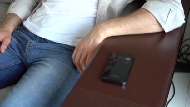 Uśmiechnięty mężczyzna dzwoni do osoby, słuchając i rozmawiając ze smartfonem w salonie — Wideo stockowe