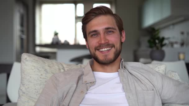 Портрет счастливого молодого человека, улыбающегося дома, отдыхающего на диване. — стоковое видео