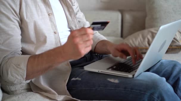 Молодий чоловік робить онлайн покупки через ноутбук, тримає кредитну картку, платить за покупки в інтернет-магазині — стокове відео