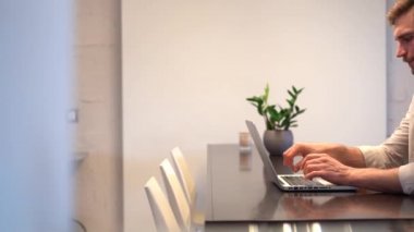 Focused business man entrepreneur typing on laptop doing research, using computer sitting at home office desk