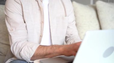 Freelancer using laptop device leaning on sofa at home, entrepreneur working distantly typing on notebook in apartment