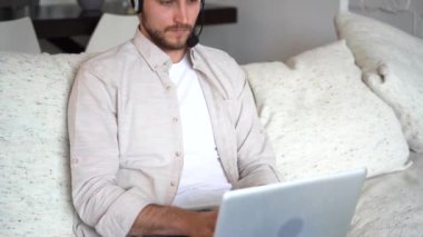 Freelancer using laptop device leaning on sofa at home, entrepreneur working distantly typing on notebook in apartment