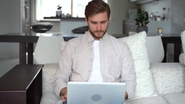 Фрілансер, використовуючи ноутбук пристрій, що спирається на диван вдома, підприємець працює віддалено друкуючи на ноутбуці в квартирі — стокове відео