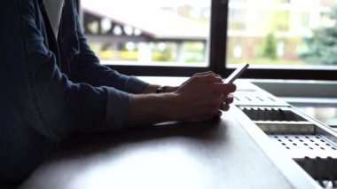 Pencerenin yanında duran gülümseyen adam akıllı telefon kullanıyor. Yakışıklı adam evde modern aletlerle vakit geçiriyor.