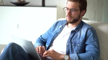 Genç adam koltukta oturur, dizüstü bilgisayar kullanır, çalışır veya uzaktan modern kablosuz teknoloji ve internet bağlantısını kullanarak çalışır.