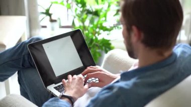 Genç adam koltukta oturur, dizüstü bilgisayar kullanır, çalışır veya uzaktan modern kablosuz teknoloji ve internet bağlantısını kullanarak çalışır.