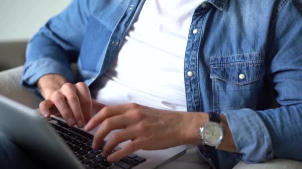 Großaufnahme männlicher Hände beim Tippen auf dem Laptop. Junger Mann sitzt mit Laptop im Wohnzimmer und arbeitet drinnen — Stockvideo