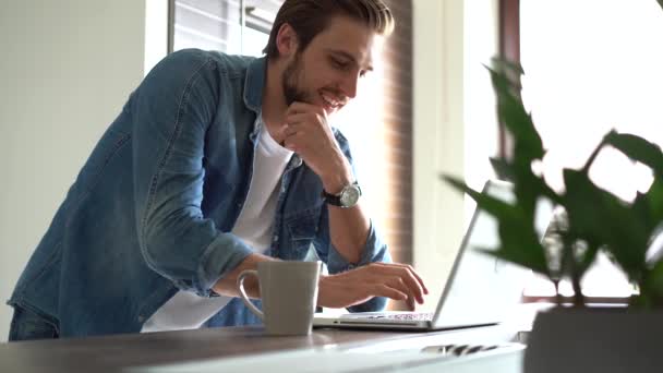 Homem sorridente com óculos trabalha em casa em sua cozinha usando um laptop. Trabalho remoto e aprendizagem remota. — Vídeo de Stock
