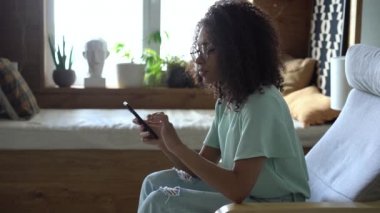 Rahat bir ırk kadını sosyal medyada akıllı telefon kullanıyor, haberleri kontrol ediyor ya da koltukta oturan mesajları kontrol ediyor.