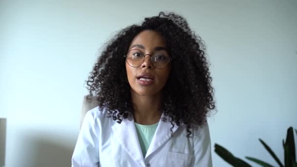 Жінка-лікар змішаної раси, яка консультує онлайн-пацієнта через відеодзвінок, дивлячись на камеру, що розмовляє камерою, робить відео чат на відстані — стокове відео