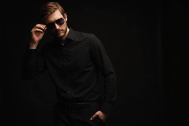 Men in full suit. Confident young businessman in sunglasses standing isolated on black.