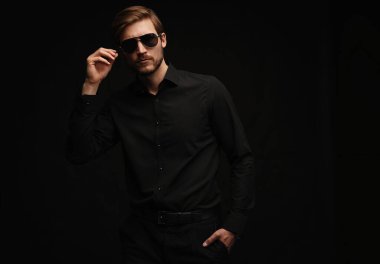 Men in full suit. Confident young businessman in sunglasses standing isolated on black.