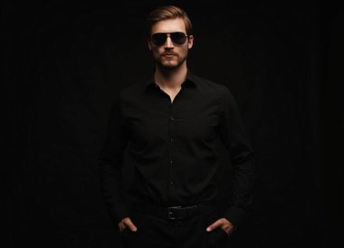 Men in full suit. Confident young businessman in sunglasses standing isolated on black.