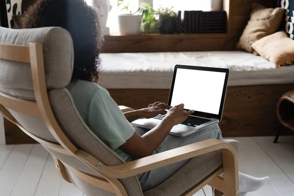 Mujer de raza mixta trabajando en computadora portátil con pantalla blanca en blanco en casa, sentado en la silla, sobre el hombro — Foto de Stock