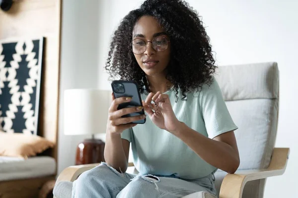 Beautiful Young Mixed race Woman Using Smartphone, while Sitting on the Chair, Surfs Internet, Posts on Social Media — Stok Foto