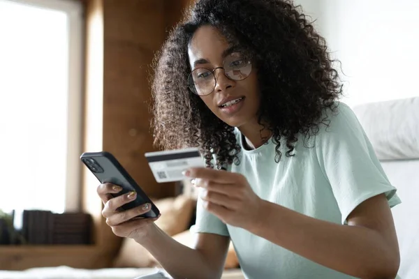 Feliz millennial mixta mujer de raza con tarjeta de crédito bancaria, la introducción de información de pago en la aplicación de teléfono inteligente — Foto de Stock