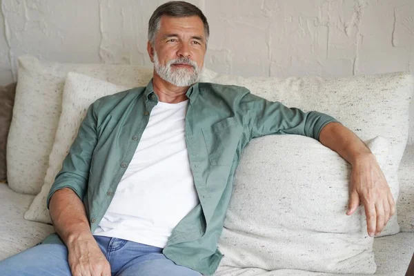 Portrait of attractive senior man sitting in sofa at home. — Foto Stock