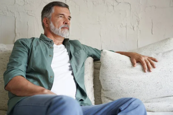 Portrait of attractive senior man sitting in sofa at home. — Stockfoto