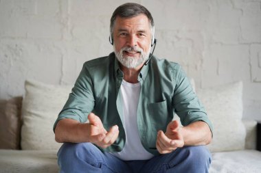 Olgun bir adam kanepeye oturmuş kameraya bakıyor ve internet kamerası uygulaması kullanarak uzaktan sohbet ediyor.