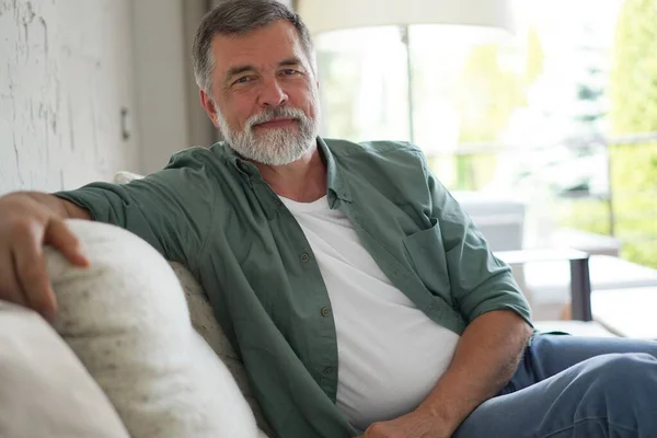 Portrait of attractive senior man sitting in sofa at home. — Stockfoto