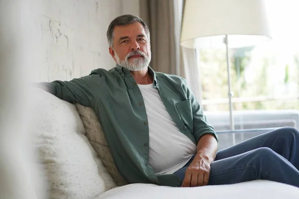 Portrait of attractive senior man sitting in sofa at home. — Stockfoto