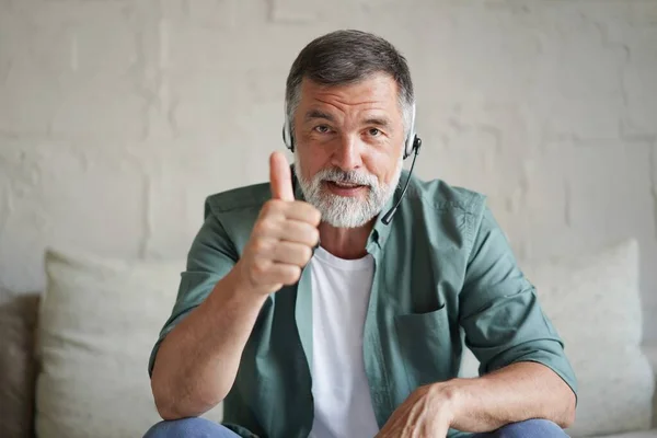 Mature man sitting on couch looking at camera having distant conversation using web camera online application — Stockfoto
