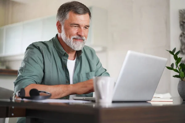 Snygg mogen man i ledig kostym sitter vid bordet i hemmakontoret och arbetar på laptop — Stockfoto