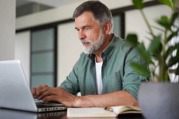 Snygg mogen man i ledig kostym sitter vid bordet i hemmakontoret och arbetar på laptop — Stockfoto