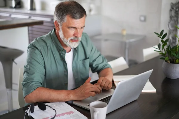 Snygg mogen man i ledig kostym sitter vid bordet i hemmakontoret och arbetar på laptop — Stockfoto