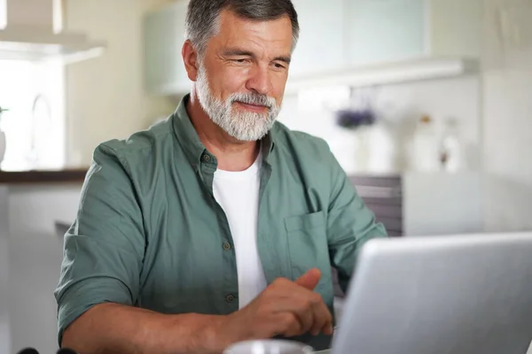 Hombre maduro guapo en traje casual sentado en la mesa en la oficina en casa y trabajando en el ordenador portátil — Foto de Stock