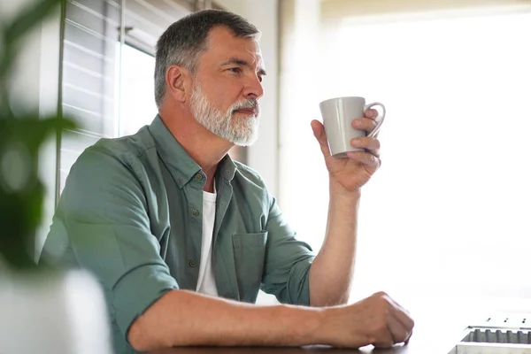 Feliz hombre maduro bebiendo café en casa en la cocina, disfrutando de una bebida caliente en la mañana del fin de semana — Foto de Stock