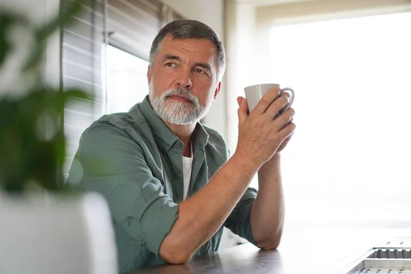 Gelukkig volwassen man drinken koffie thuis in de keuken, genieten van warme drank in de ochtend in het weekend — Stockfoto