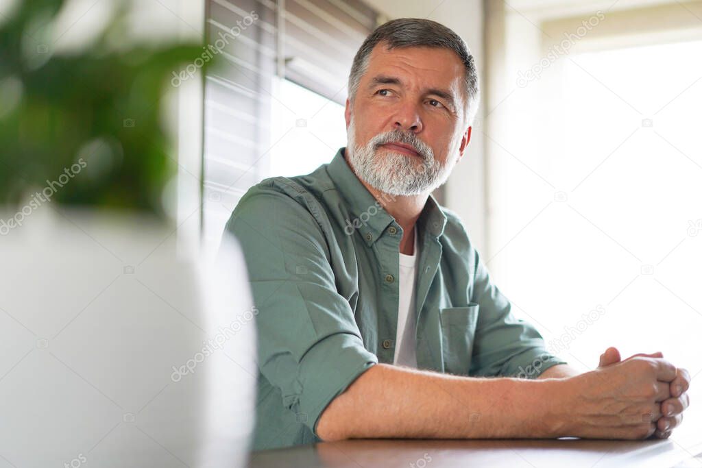 Happy attractive mature man sitting at table in kitchen.