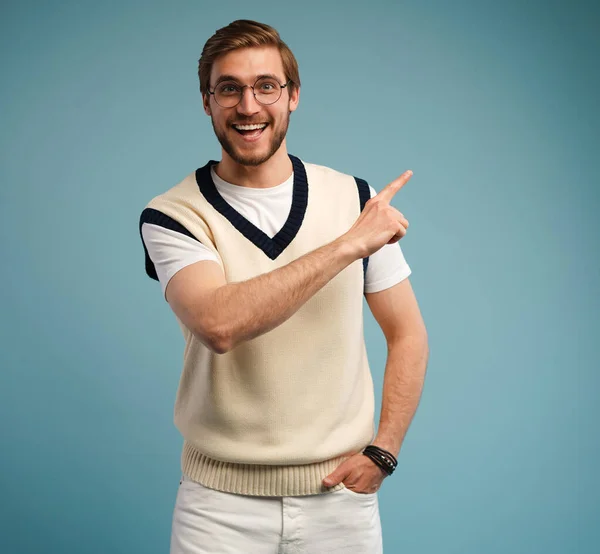 Portrait of a happy young man in casual pointing fingers away at copy space isolated over blue background. — Stock Photo, Image