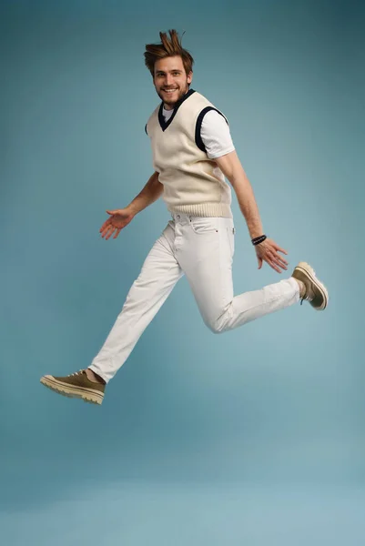 Full length portrait of an excited young man in white t-shirt jumping while celebrating success isolated over blue — Stock Photo, Image
