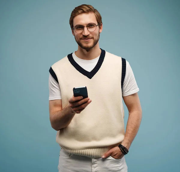 Glücklicher Mann mit Brille tippt SMS auf blauem Hintergrund. — Stockfoto