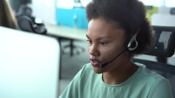Mujer afroamericana de raza mixta con auriculares que utilizan ordenador, hablando, operador de servicio de atención al cliente de trabajo — Vídeo de stock