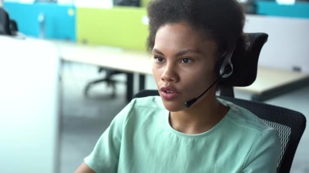 Femme afro-américaine de race mixte avec casque utilisant l'ordinateur, parler, opérateur de service de soutien à la clientèle de travail — Video