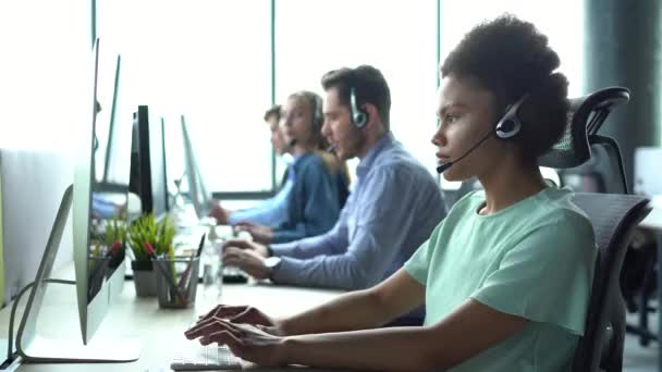 Mujer afroamericana de raza mixta con auriculares que utilizan ordenador, hablando, operador de servicio de atención al cliente de trabajo — Vídeos de Stock